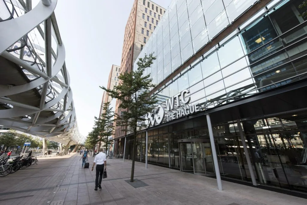 Ingang van WTC The Hague aan de Prinses Beatrixlaan met moderne architectuur en wandelende voetgangers.